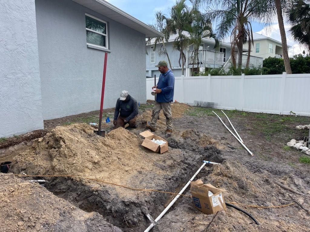 Two men are digging in the dirt in front of a house.