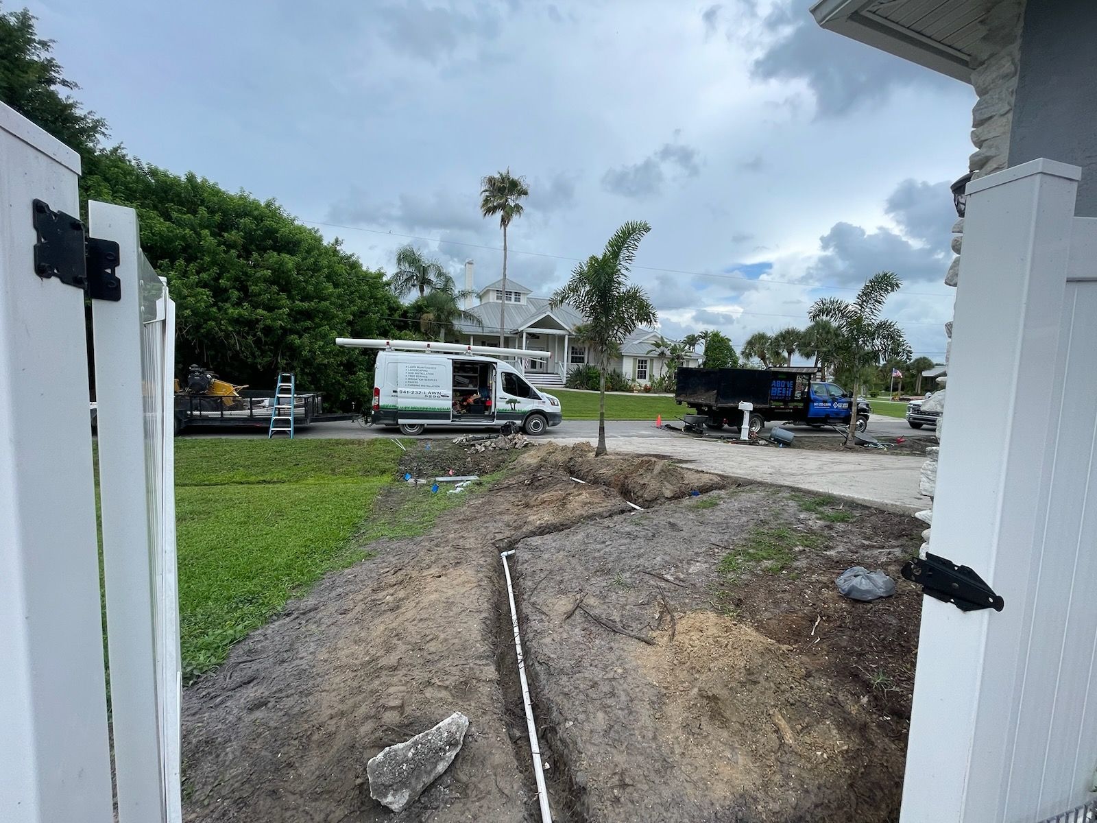 A white van is parked on the side of the road next to a white fence.