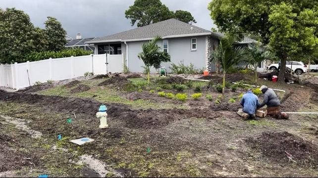 Two men are kneeling in the dirt in front of a house.