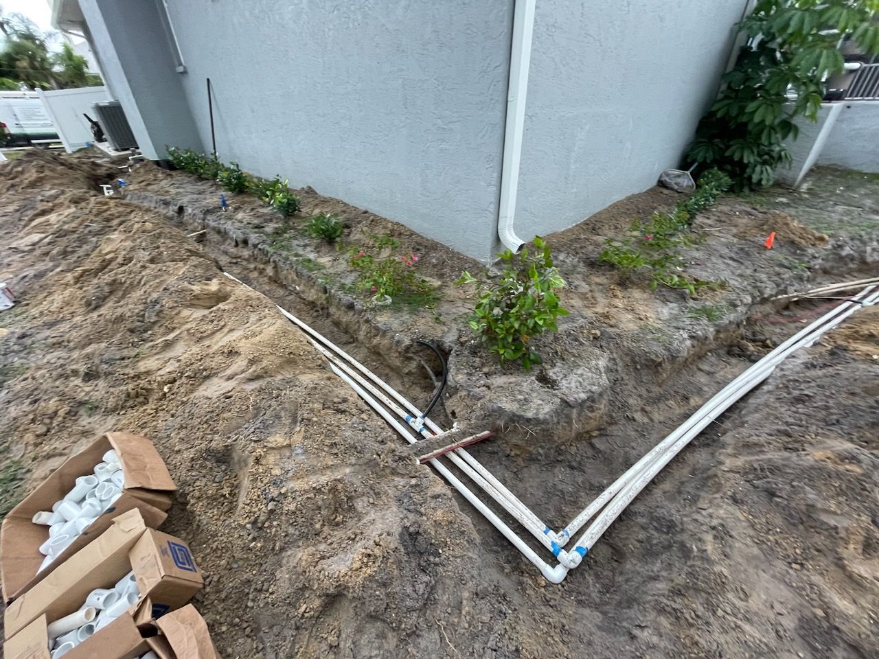 A bunch of pipes are laying in the dirt next to a house.