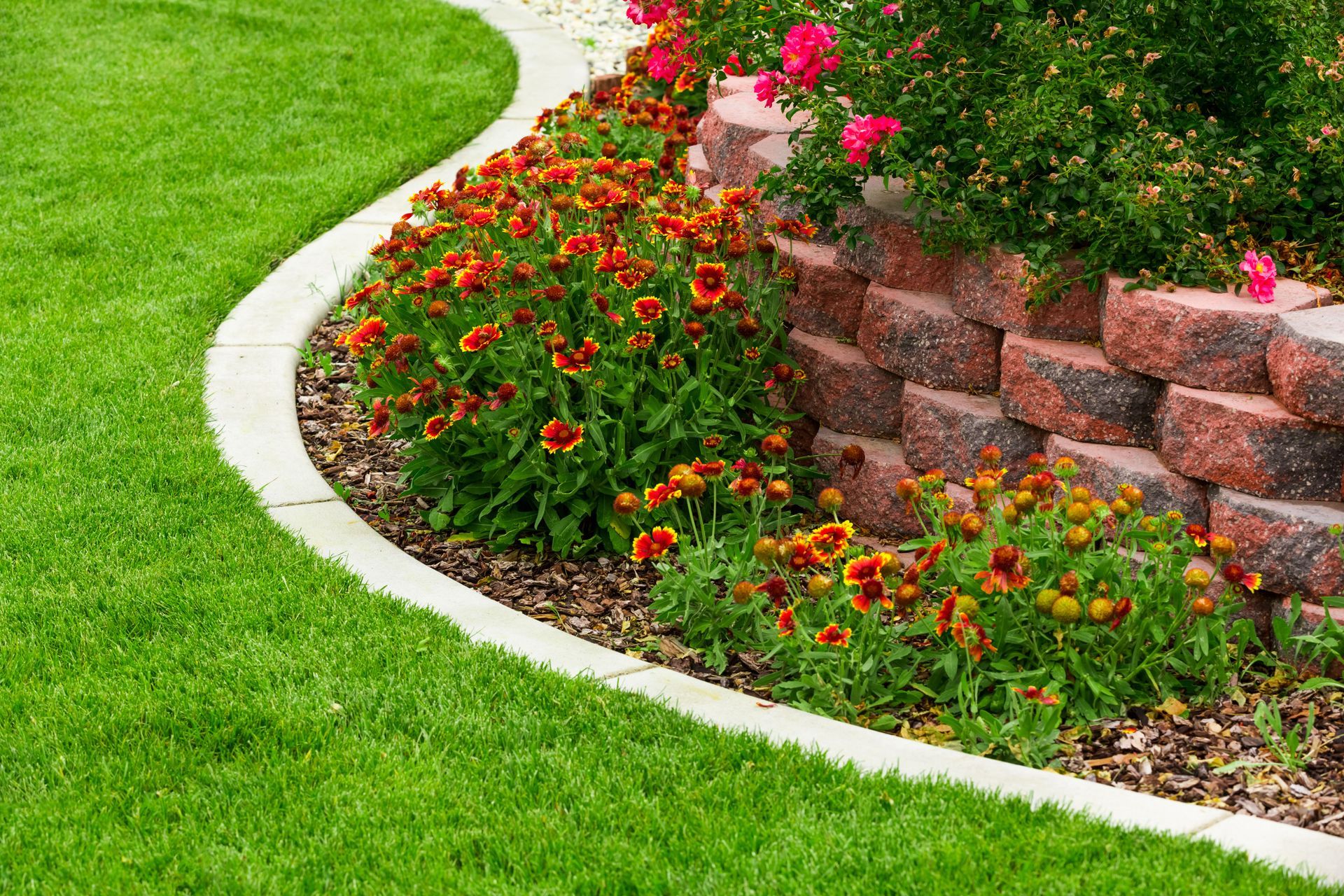 A lush green lawn with flowers and a stone wall