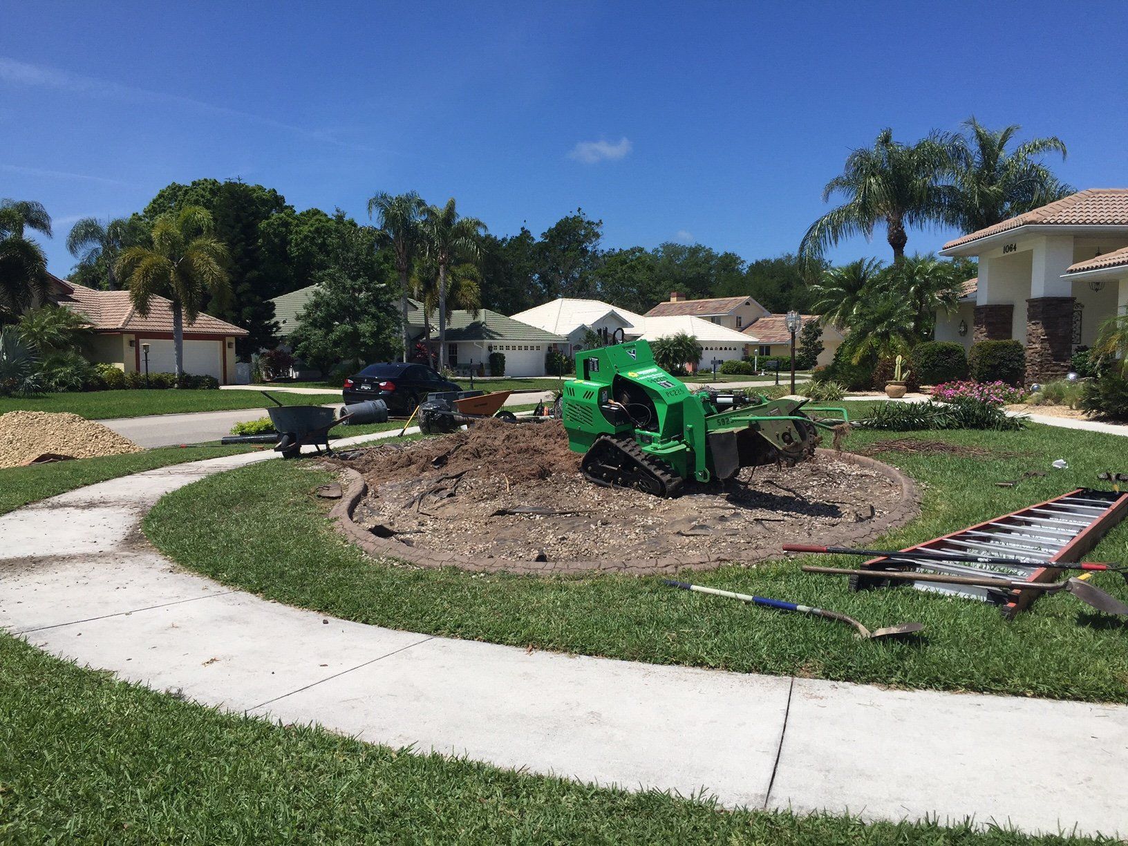 A green tractor is working on a tree stump in a yard.