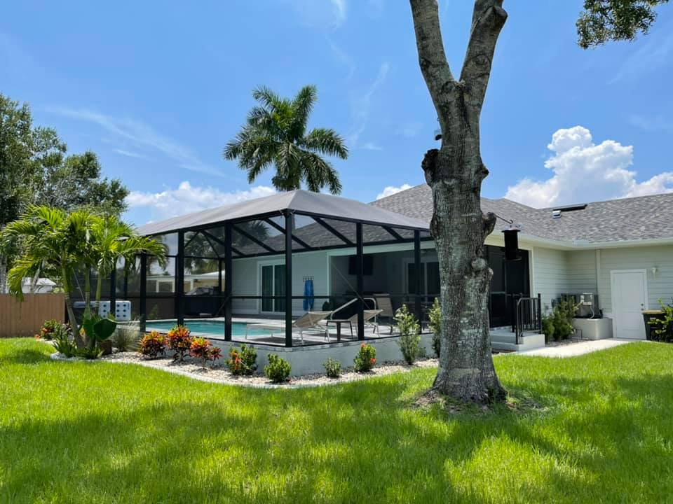 A house with a screened in pool and a tree in the backyard.