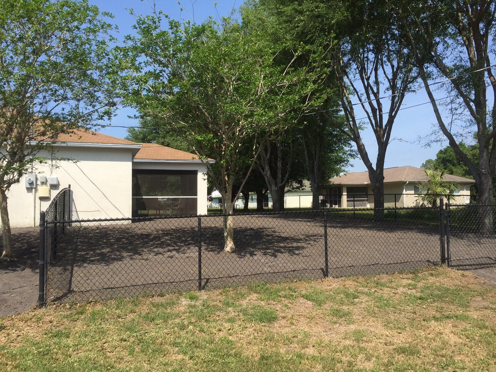 A chain link fence surrounds a yard with a house in the background.