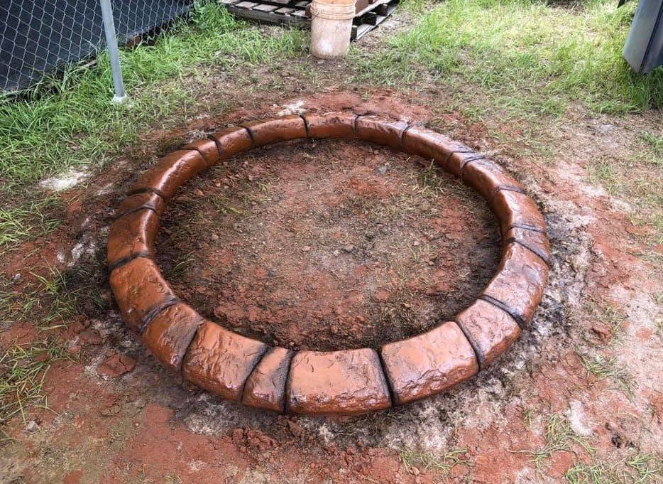 A fire pit is being built in the dirt in a backyard.