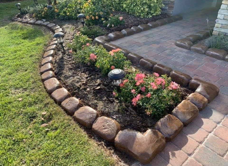 A garden with flowers and brick edging in front of a house.