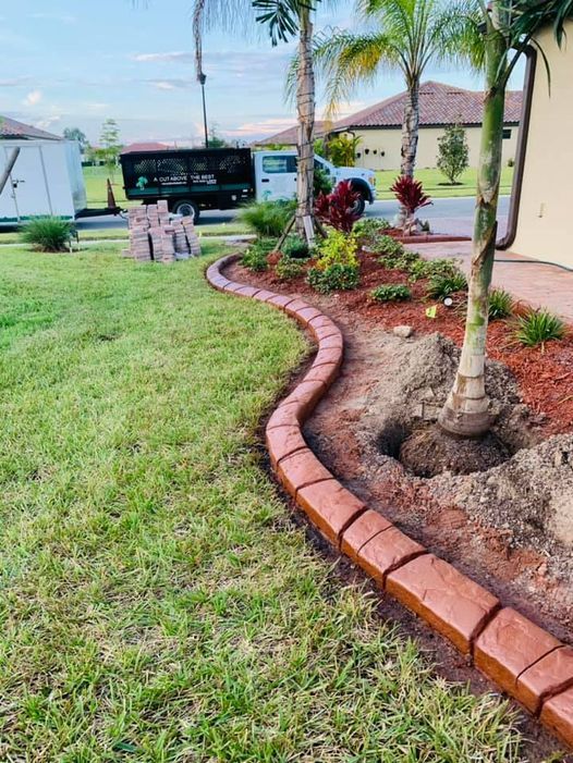 A brick curb is being installed in a lush green yard.