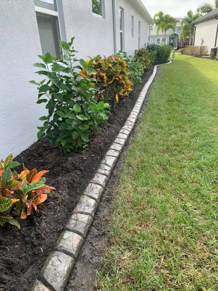 A lawn with a brick curb and plants in front of a house.