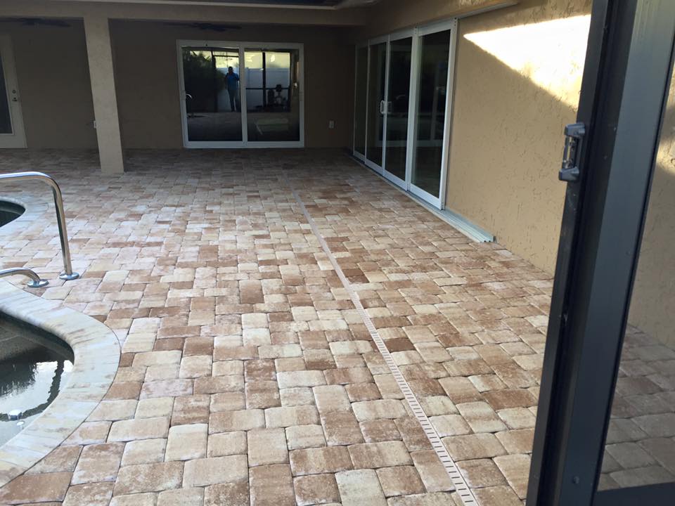 A patio with bricks and sliding glass doors next to a pool.