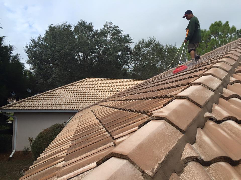A man is cleaning the roof of a house with a broom.