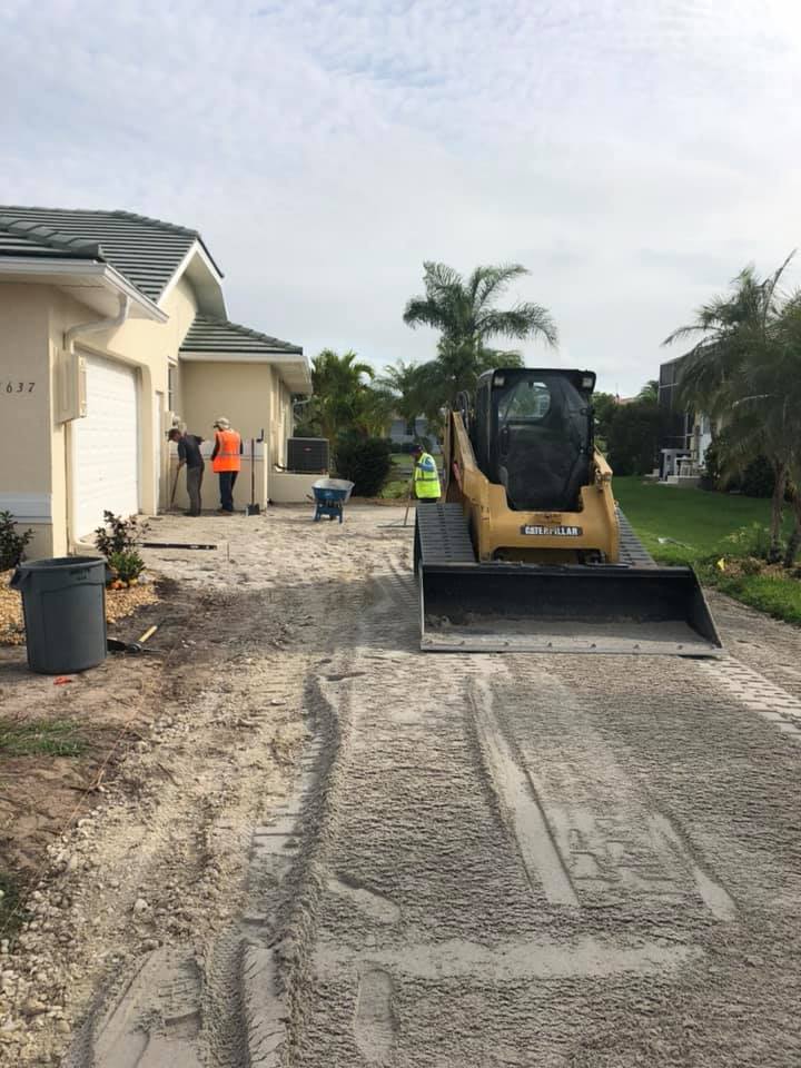 A bulldozer is driving down a dirt road in front of a house.