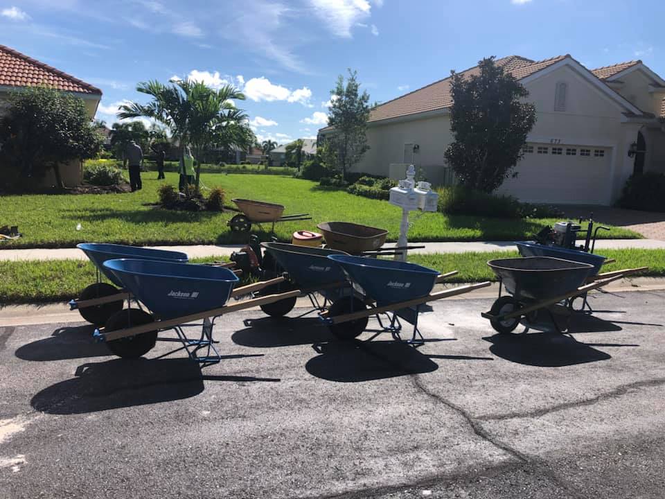 Three wheelbarrows are parked on the side of the road in front of a house.