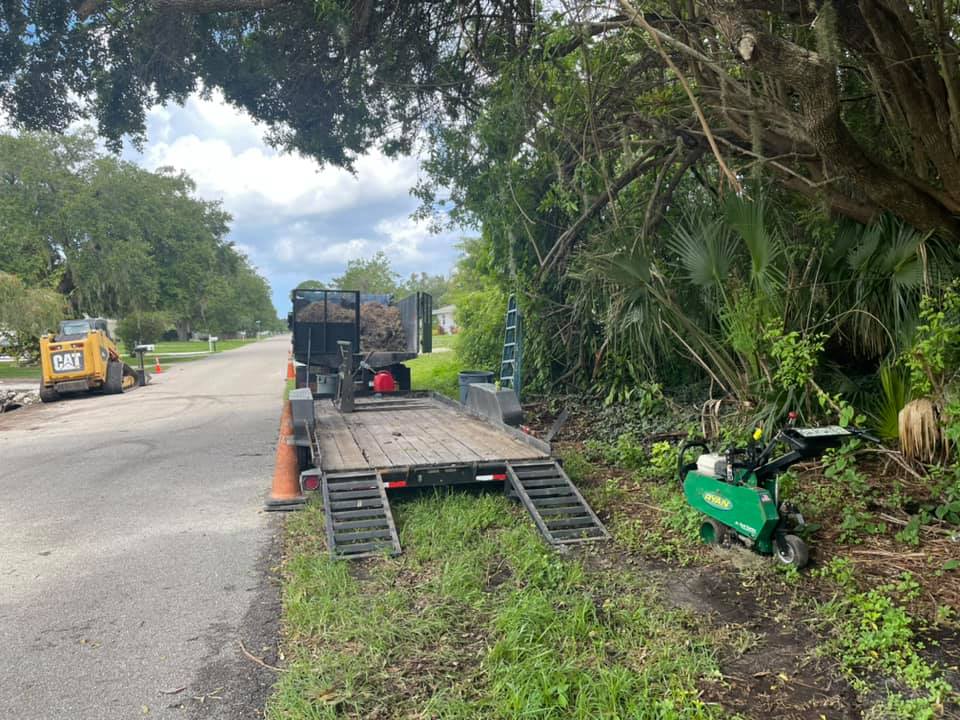 A trailer with a tractor on it is parked on the side of the road.