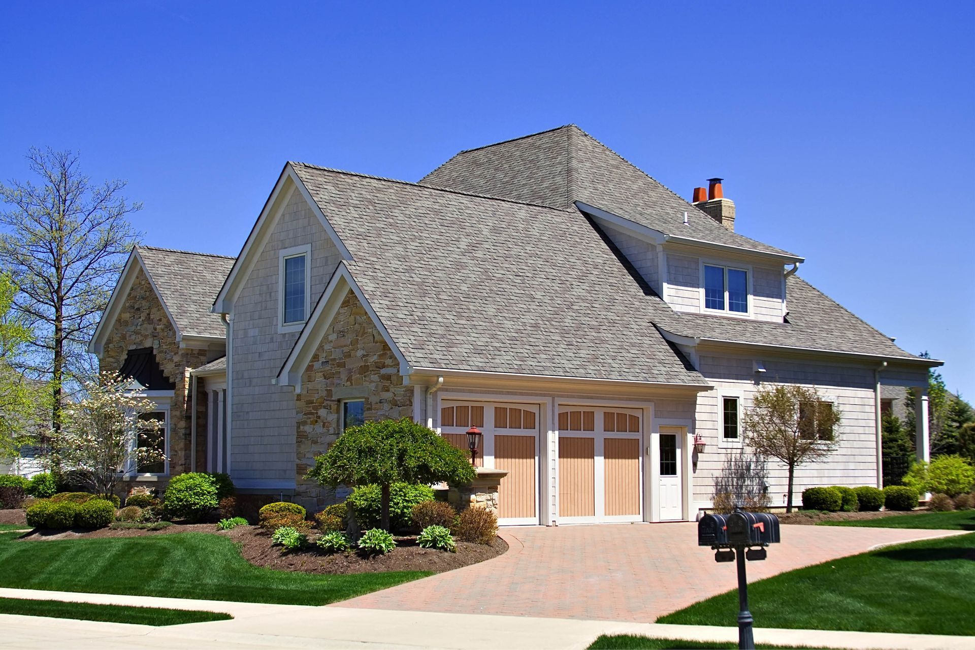 Two-story house with gray roof, beige siding, stone accents, and light wooden garage doors.