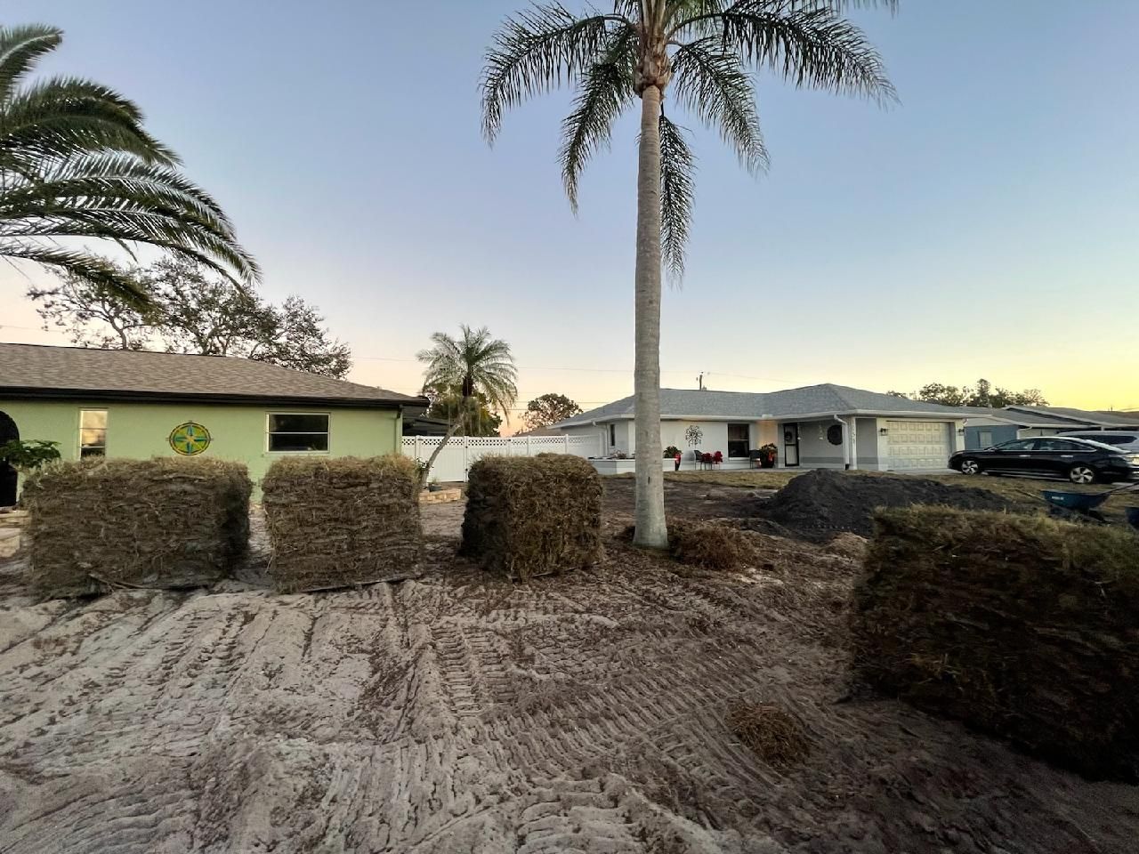 A pile of hay is sitting in front of a house with a palm tree in the background.