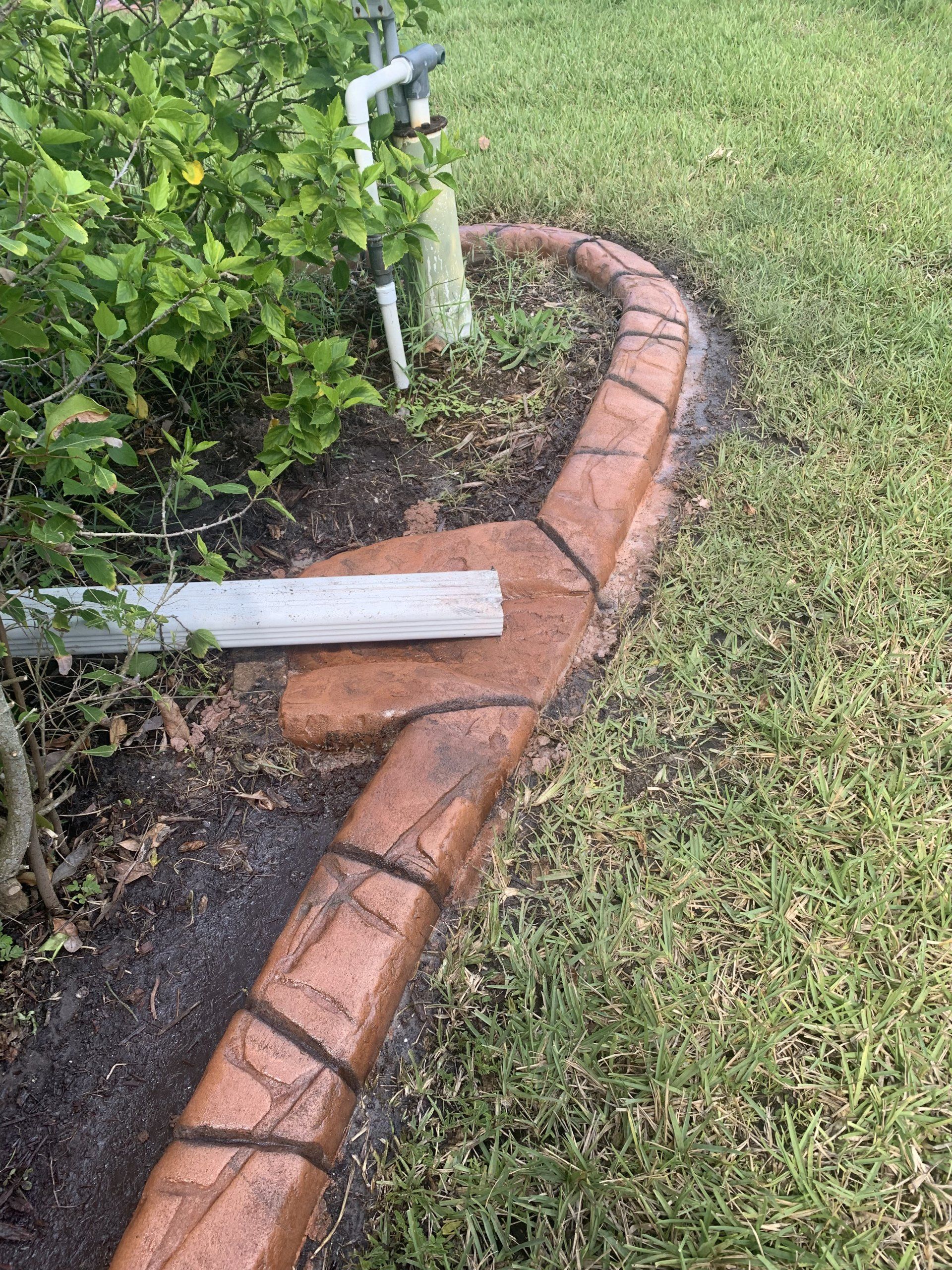 A concrete curb is being installed in a yard next to a bush.