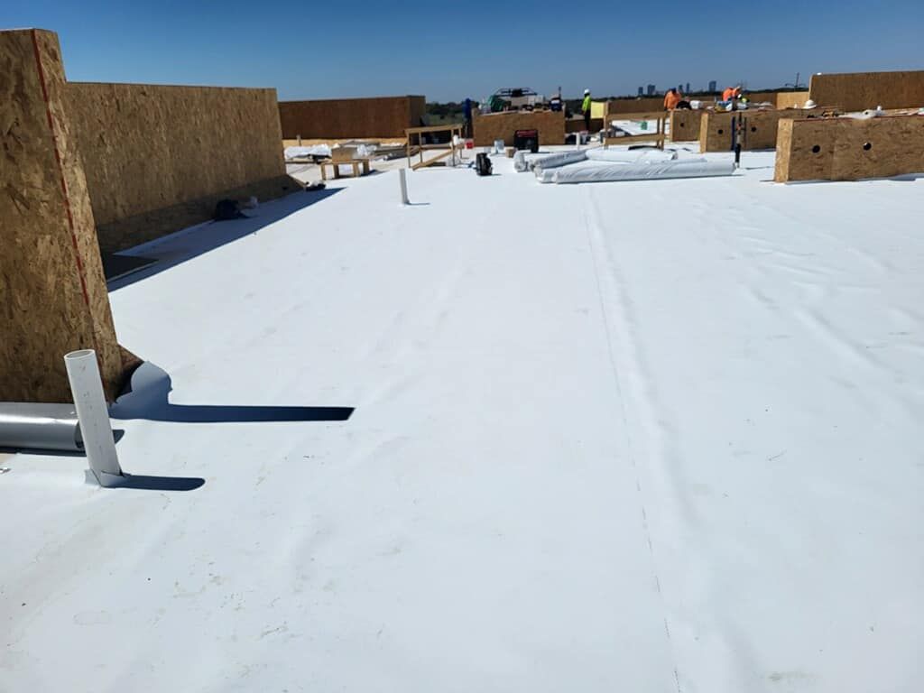 White roof with building materials and construction workers on a sunny day.