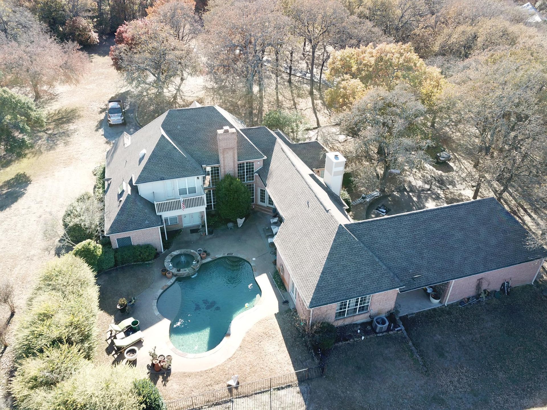Aerial view of a large brick house with a pool, patio, and surrounding trees.