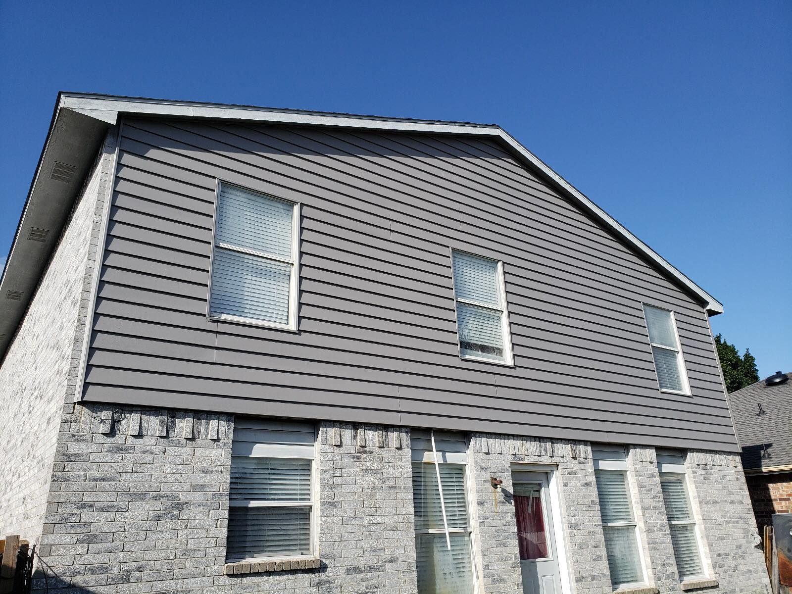 Two-story house with gray siding above gray brick. Three windows on the upper floor.