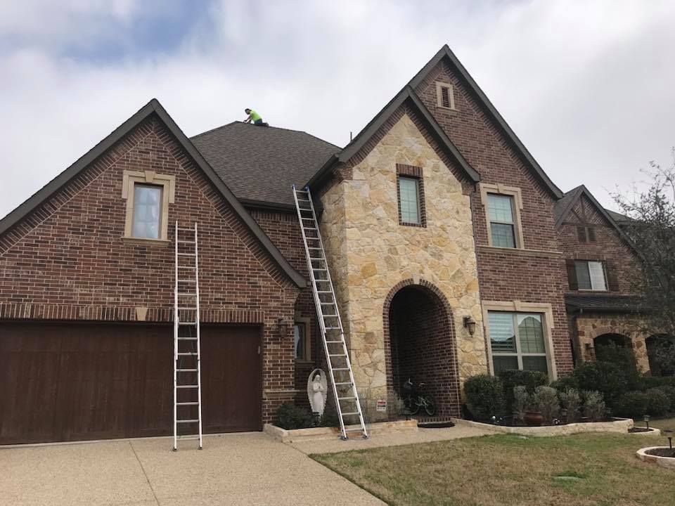 Two ladders against a brick house with a person working on the roof.