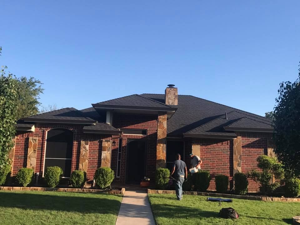 Brick house with black roof, person walks toward the entrance, green lawn and clear blue sky.