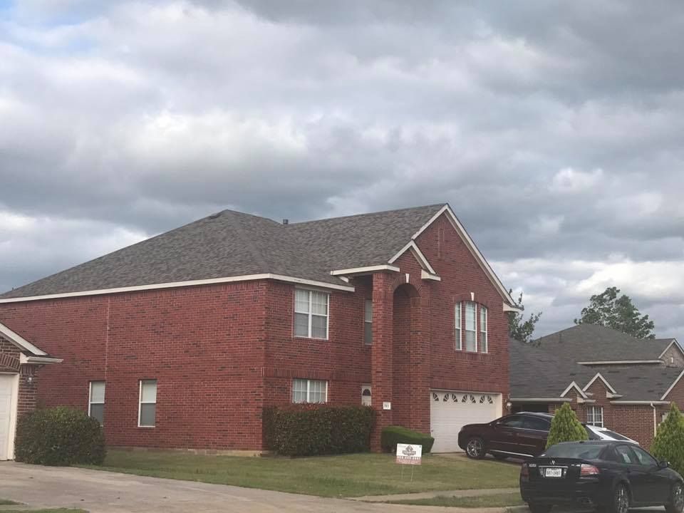 Brick house with gray roof, parked cars, and cloudy sky.