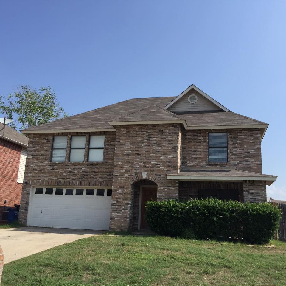 Two-story brick house with a white garage door, green lawn, and blue sky.