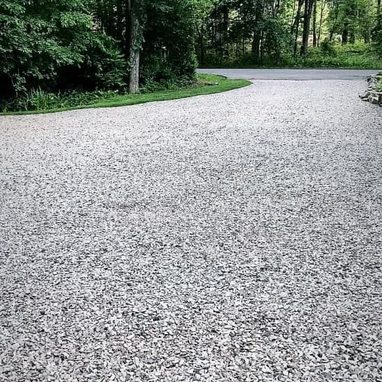 A gravel driveway leading to a road with trees in the background.