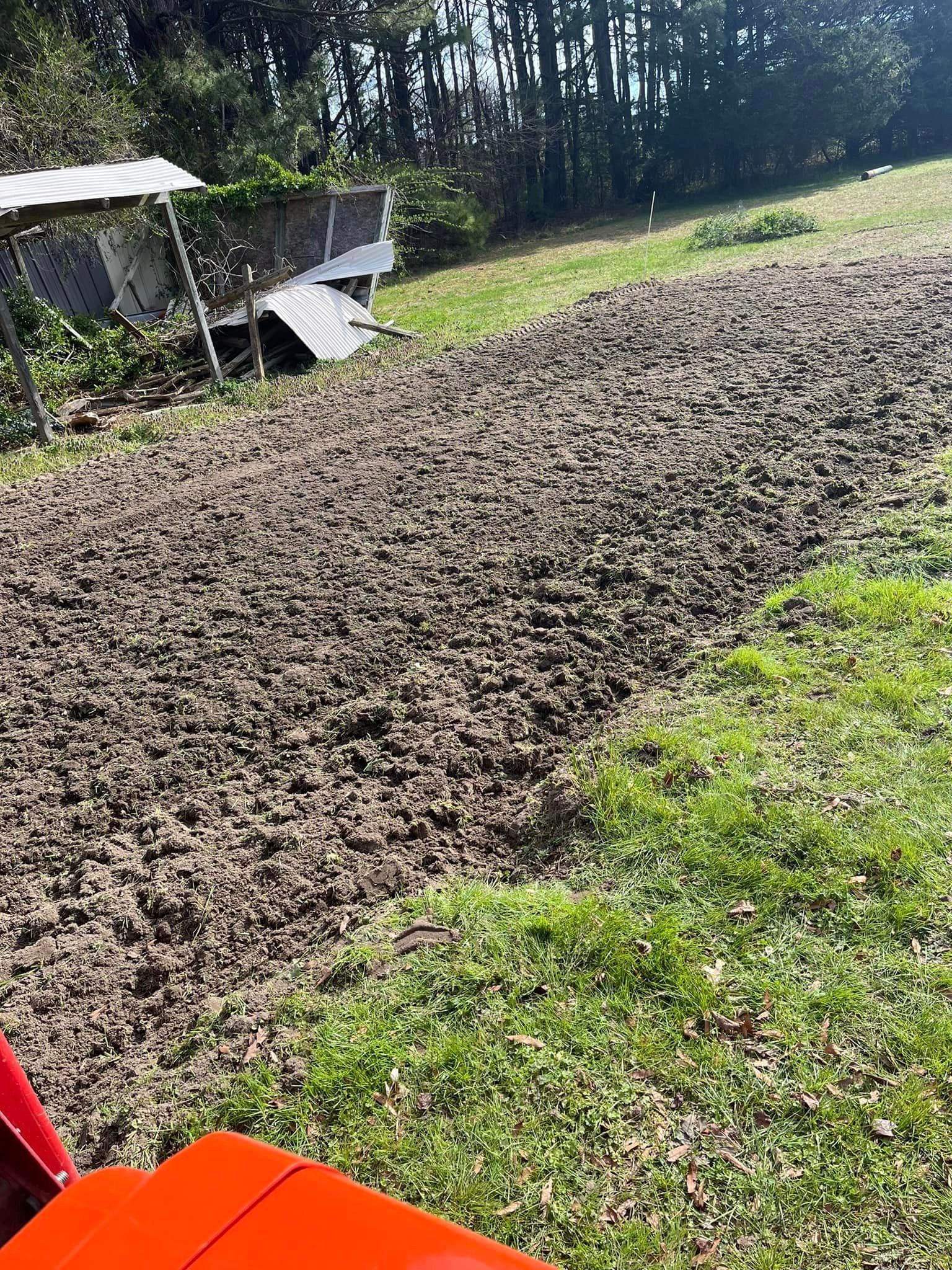 A tractor is plowing a field of dirt and grass.