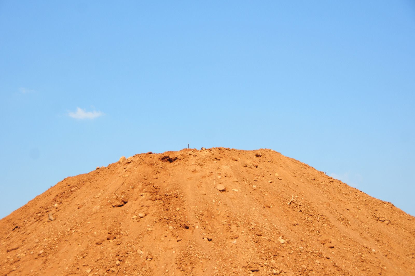 A large pile of dirt against a blue sky.