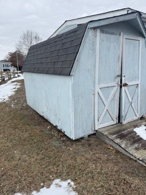 A white shed with a black roof is sitting in the middle of a field.