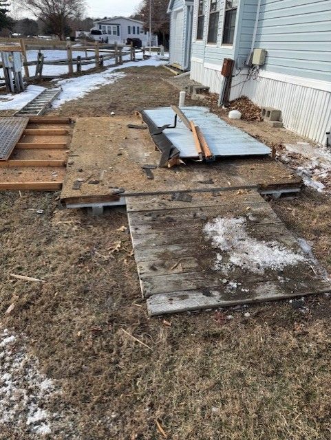 A lot of wooden boards are laying on the ground in front of a house.