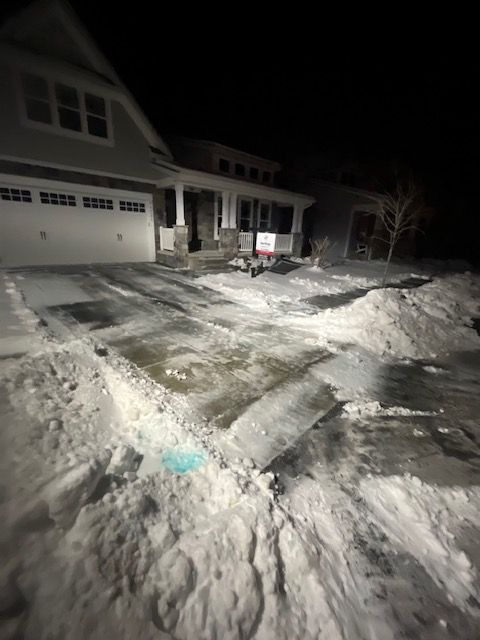 A snowy driveway in front of a house at night.