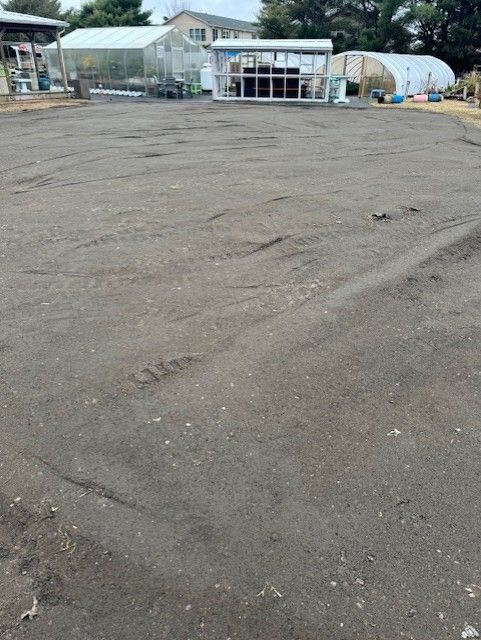 A large empty parking lot with a greenhouse in the background