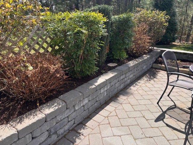 A brick patio with a table and chairs next to a stone wall.