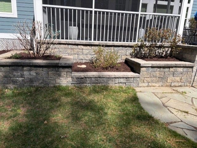 A brick wall with planters in front of a screened in porch.