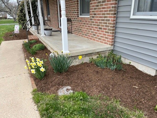 A brick house with a porch and flowers in front of it.