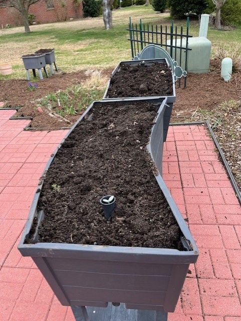A row of planters filled with dirt on a brick patio.