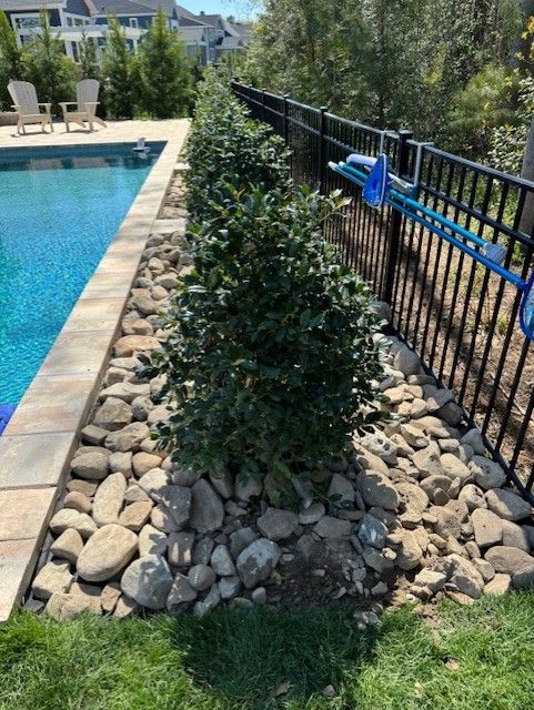 A black fence surrounds a swimming pool surrounded by rocks and bushes.
