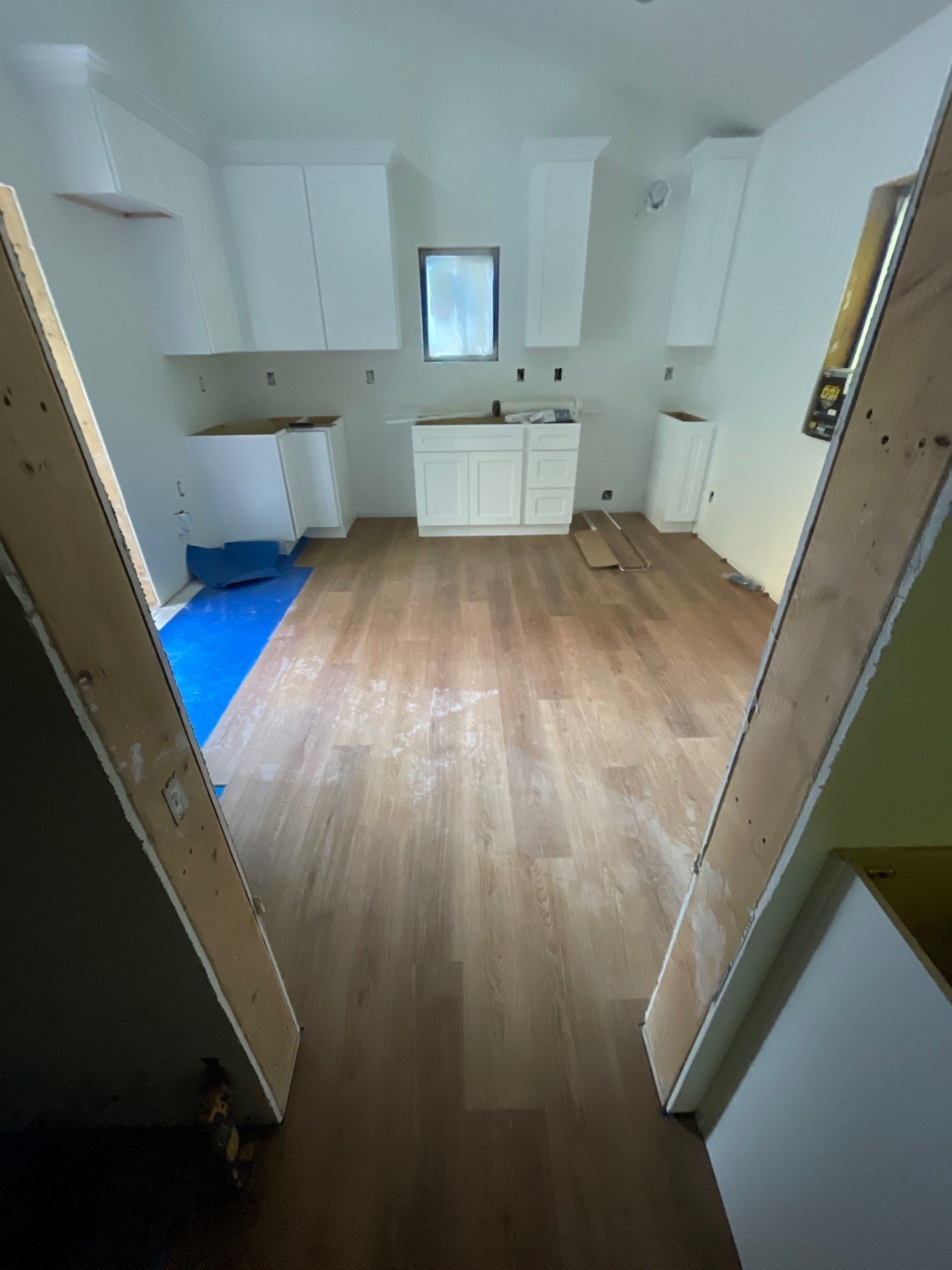 An interior view of a kitchen under renovation, featuring white cabinets, wood flooring, and unfinished doorways.