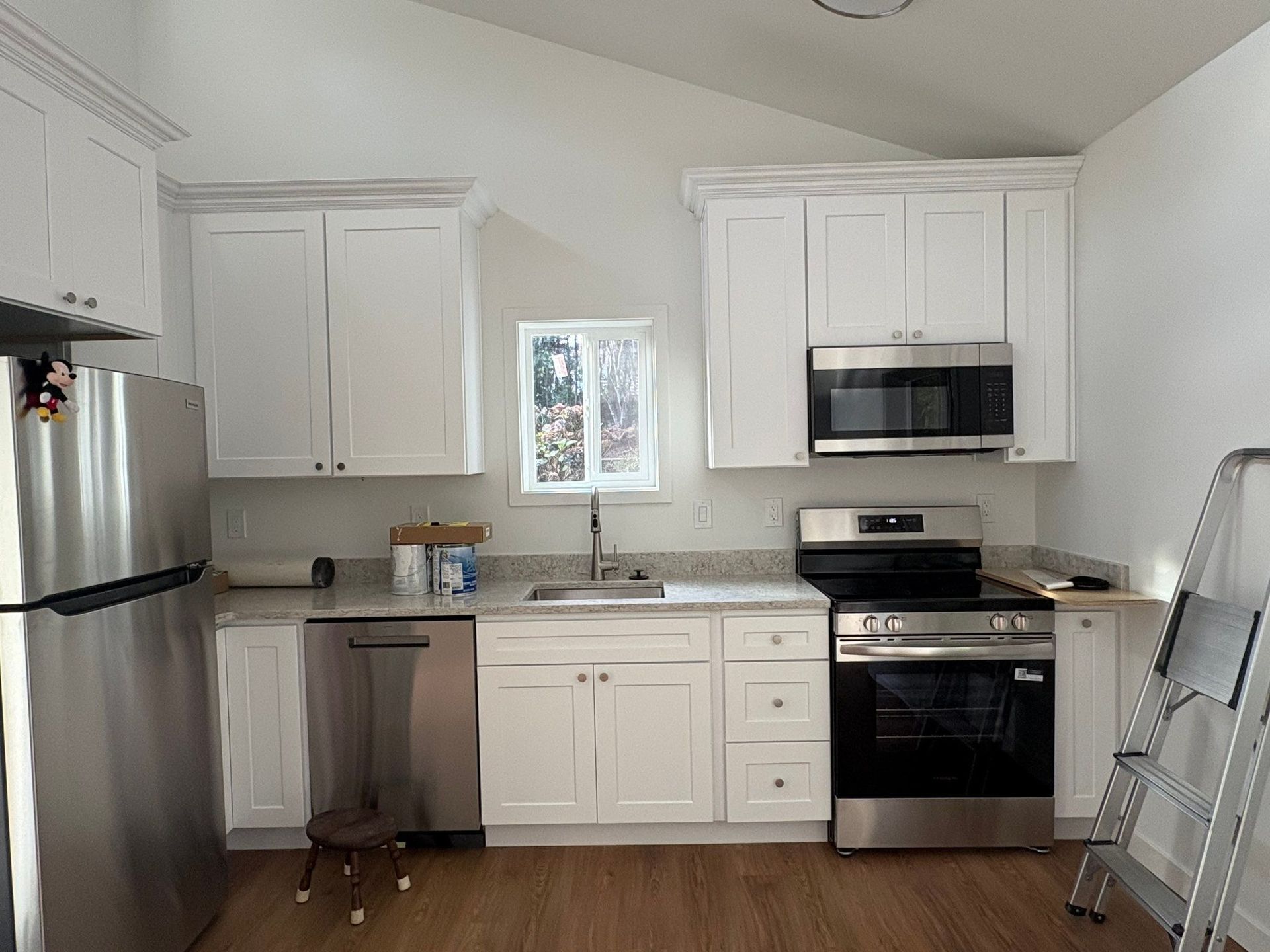 Modern kitchen featuring white cabinets, stainless steel appliances, a center sink, and wood-look flooring.