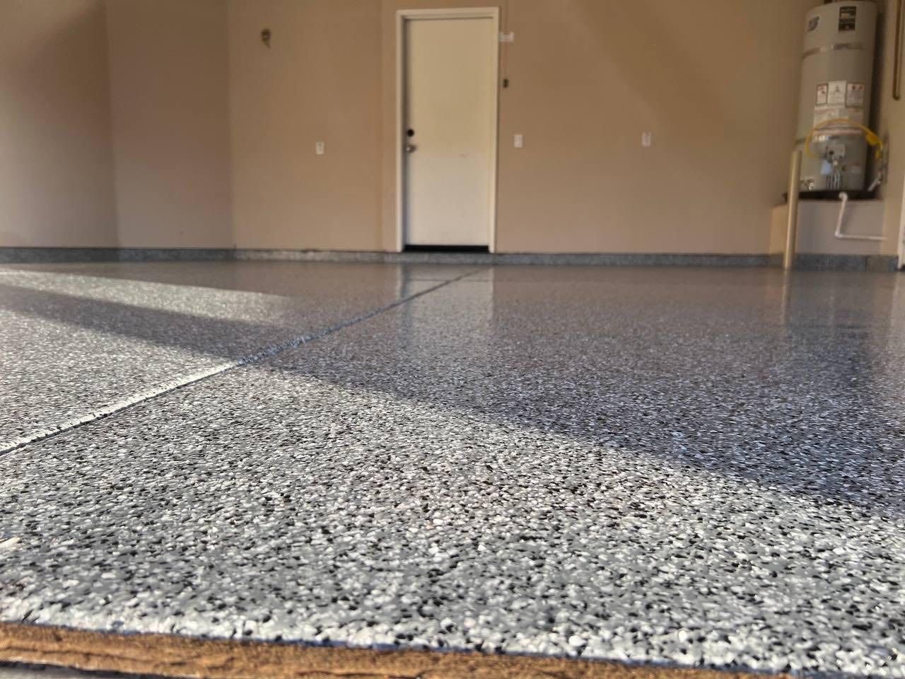 A garage with a gray, speckled epoxy floor, a white interior door, and a water heater in the corner.