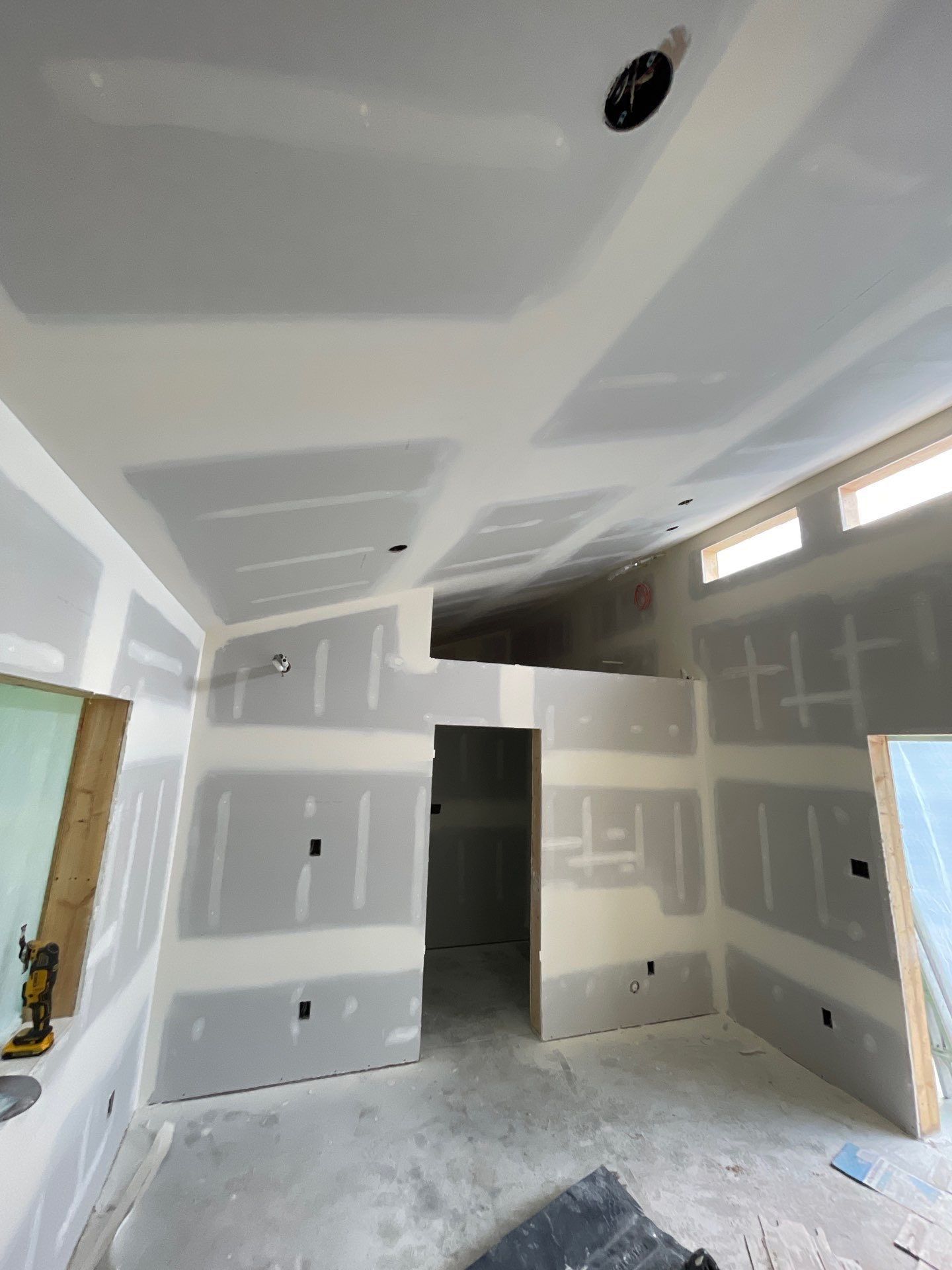 An indoor view of a kitchen under renovation featuring white cabinets, light wood-look flooring, and unfinished doorways.