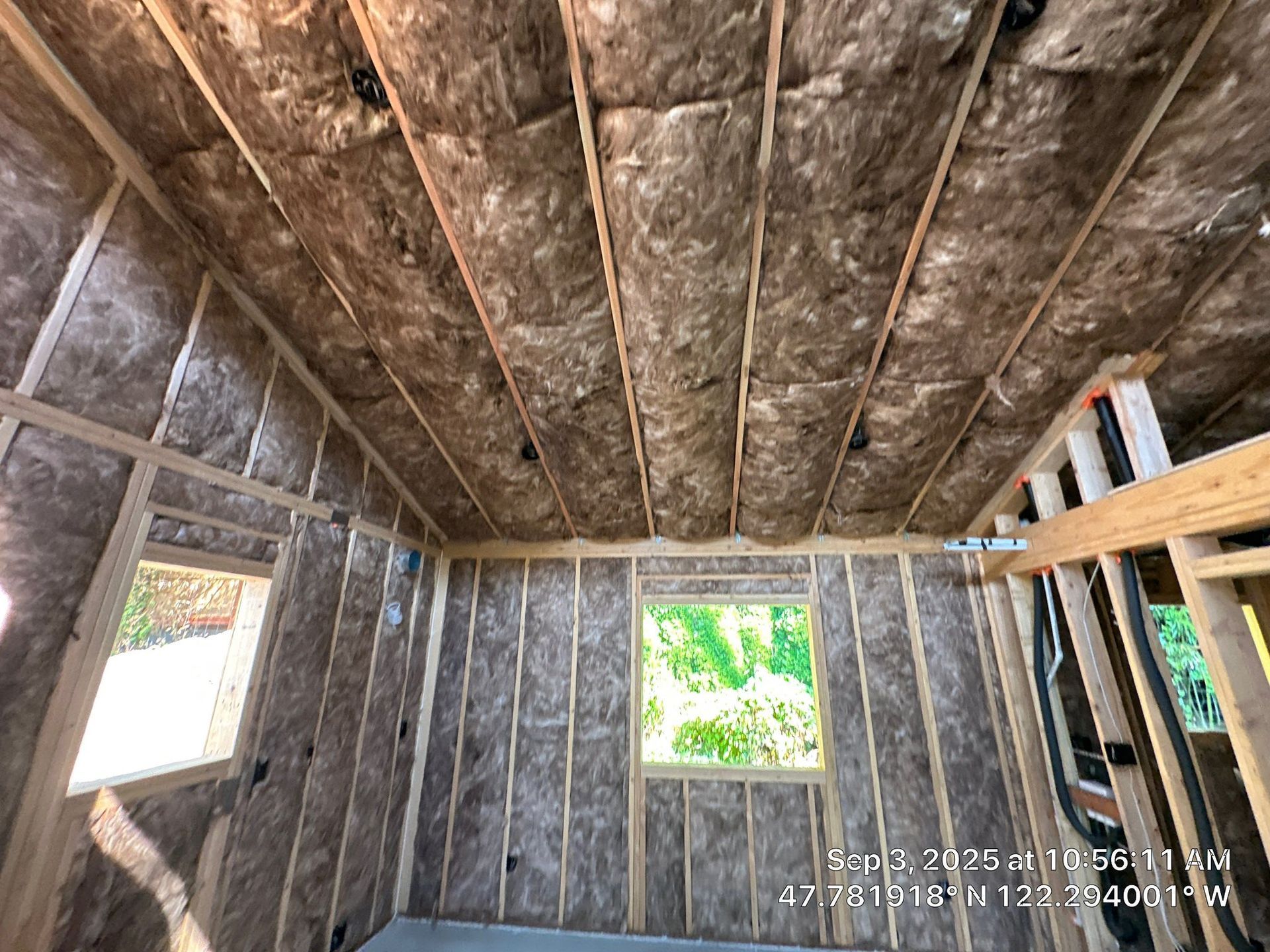 Unfinished room interior featuring exposed wooden wall studs and ceiling joists insulated with brown fiberglass batts.