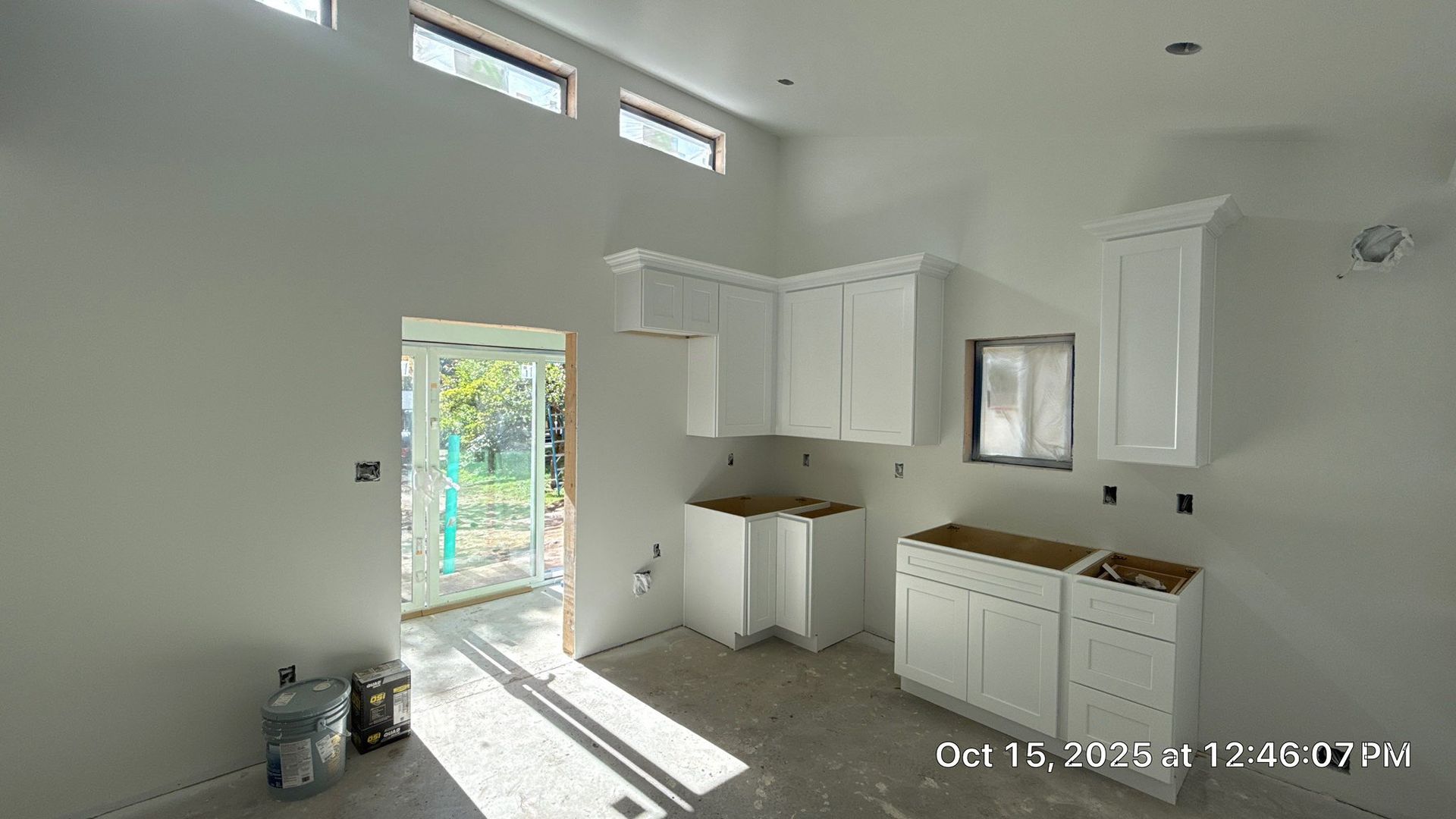 A kitchen under construction featuring white cabinets, uninstalled countertops, and tall windows on a high wall.