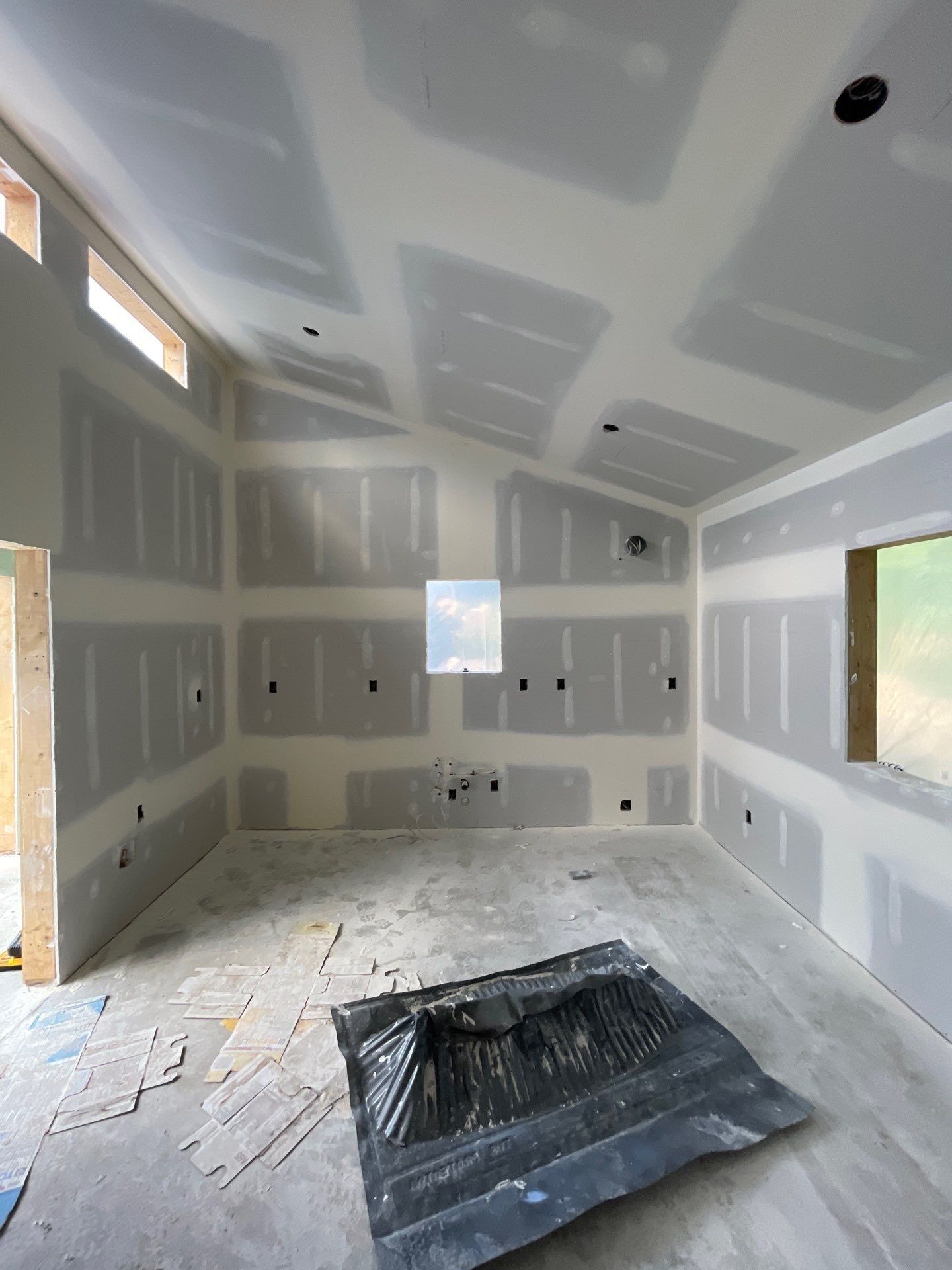 An interior room under construction with gray drywall installed on the walls and ceiling and a dark mat on the floor.
