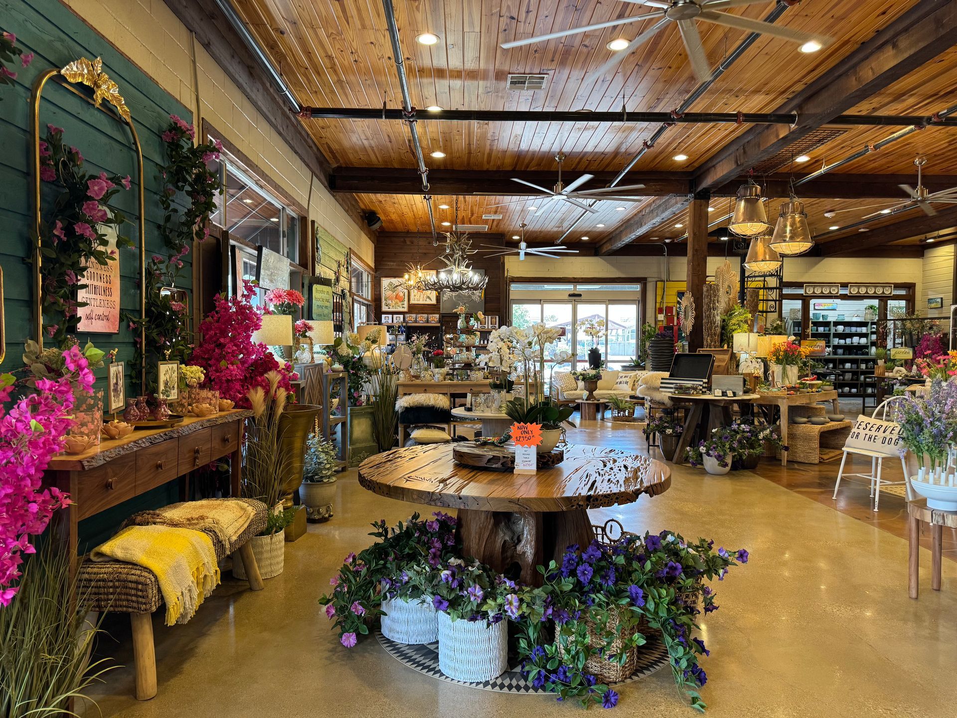 Live-edge wood round display table, artificial plants, woven baskets and blankets, wall hangings, benches, couches, mirrors, and lamps.