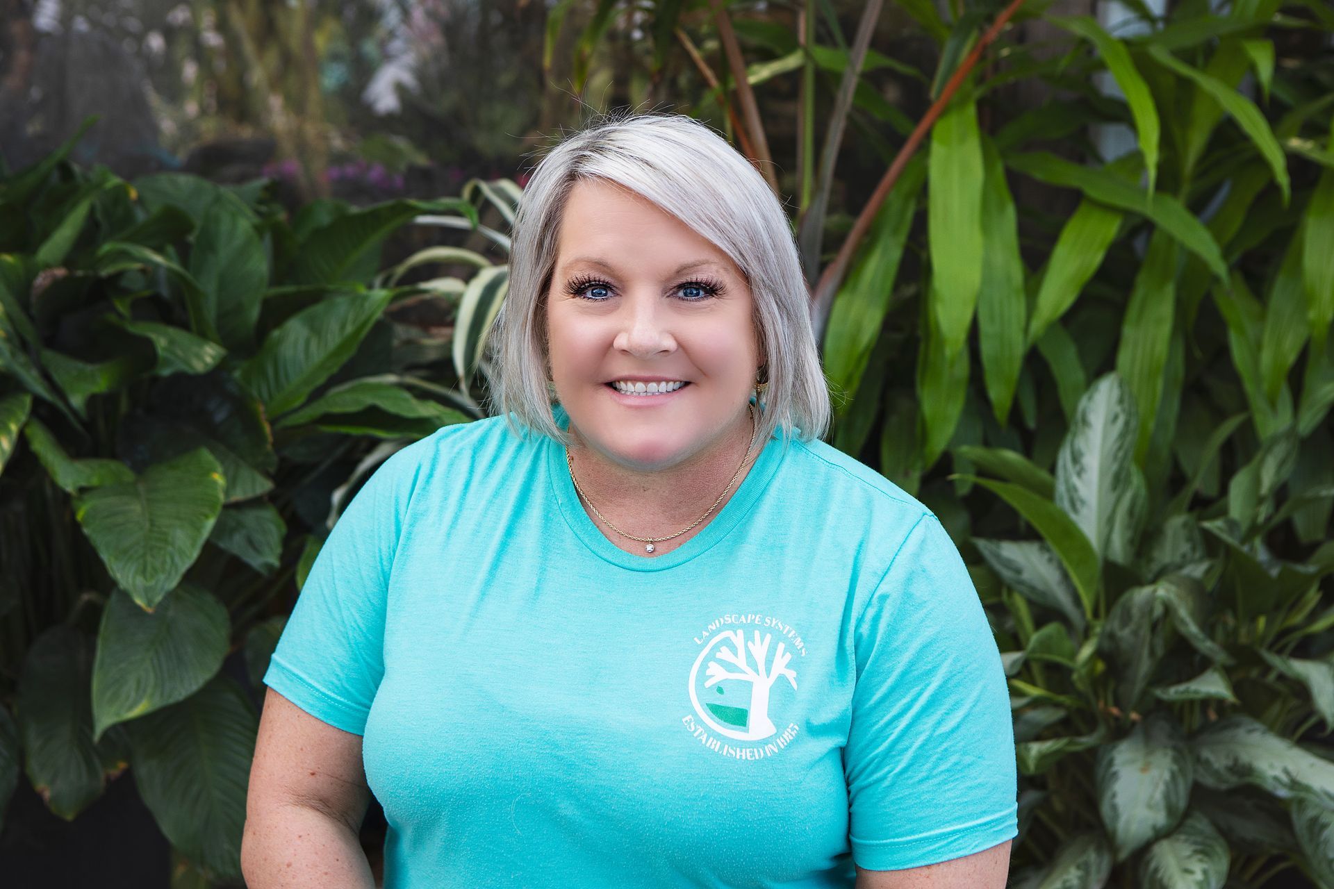 A woman in a blue shirt is standing in front of a bush.