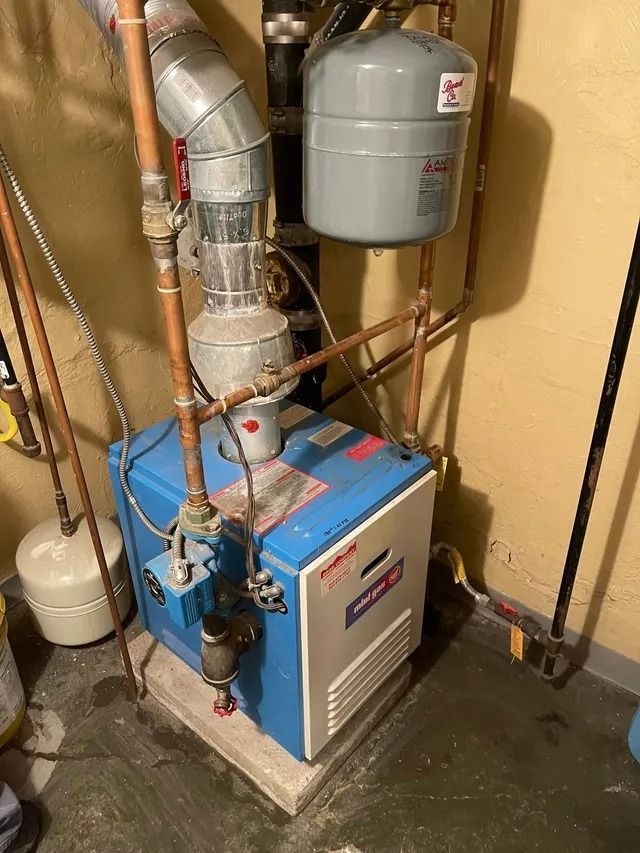 Blue and white boiler with copper pipes and expansion tank in a basement corner.