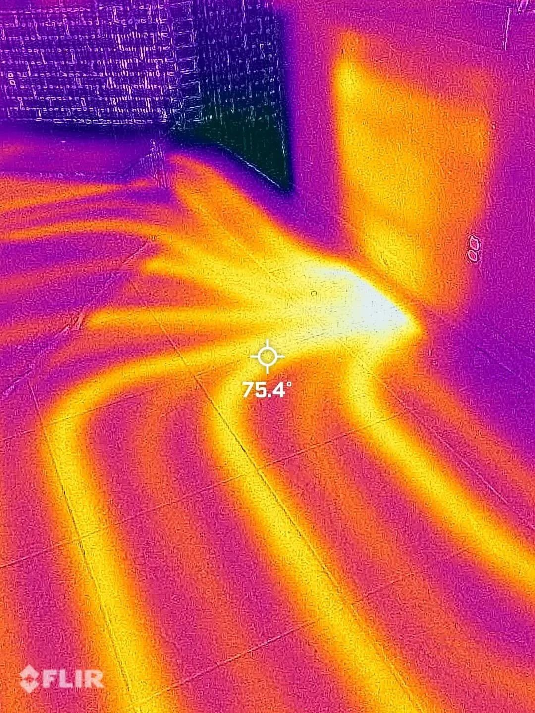Thermal image of floor and wall showing heat radiating from an unknown source. Yellow and orange hues with a temperature of 75.4 degrees.